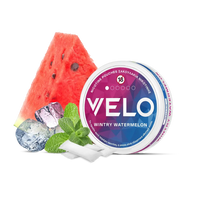 Ένα κουτί με σακουλάκια νικοτίνης VELO Wintry Watermelon βρίσκεται δίπλα σε μια φέτα καρπούζι, φύλλα μέντας, παγάκια και δύο λευκά σακουλάκια. Η ετικέτα του κουτιού είναι ροζ και μπλε.