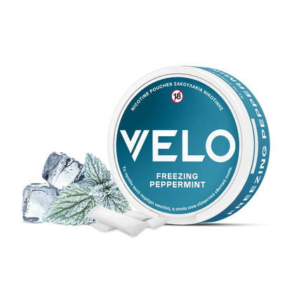 Ένα ανοιχτό στρογγυλό δοχείο VELO Freezing Peppermint προβάλλεται με δύο λευκά σακουλάκια, παγάκια και φύλλα μέντας μπροστά, αποτυπώνοντας την έντονη γεύση μενθόλης του προϊόντος.
