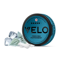 Ένα μπλε κουτάκι VELO Freezing Peppermint βρίσκεται δίπλα σε παγάκια, φύλλα μέντας και δύο λευκά σακουλάκια νικοτίνης σε λευκό φόντο, τονίζοντας τη δροσιστική γεύση μενθόλης του προϊόντος.