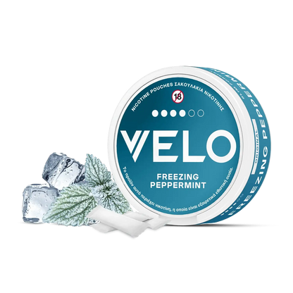 Ένα στρογγυλό μπλε και λευκό κουτί VELO Freezing Peppermint εμφανίζεται με παγάκια και φύλλα μέντας, τονίζοντας την έντονη γεύση μενθόλης. Η συσκευασία περιλαμβάνει ελληνικό και αγγλικό κείμενο καθώς και το σύμβολο προειδοποίησης ηλικίας "18+".