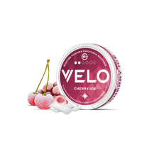 Ένα στρογγυλό δοχείο VELO Cherry Ice βρίσκεται δίπλα σε τρία παγωμένα κεράσια και δύο λευκά σακουλάκια σε μια λευκή επιφάνεια. Η ροζ και λευκή συσκευασία εμφανίζει έντονο κείμενο, τονίζοντας το προϊόν σακουλάκι νικοτίνης φυτικής προέλευσης.
