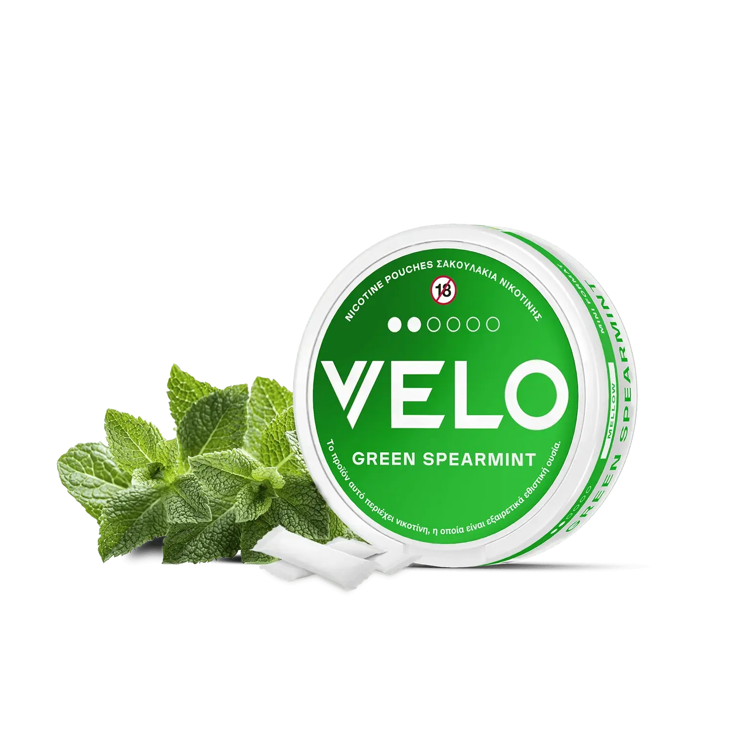 Ένα στρογγυλό λευκό δοχείο VELO Green Spearmint με πράσινες πινελιές βρίσκεται δίπλα σε φρέσκα φύλλα μέντας και σακουλάκια νικοτίνης φυτικής προέλευσης, σε απλό λευκό φόντο.