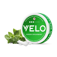 Ένα στρογγυλό πράσινο κουτί με την ένδειξη "VELO Green Spearmint" διαθέτει λευκό κείμενο, φύλλα μέντας και ένα σύμβολο "18+" στο καπάκι, επισημαίνοντας ότι πρόκειται για ένα σακουλάκι νικοτίνης μόνο για ενήλικες με φυτική βάση.