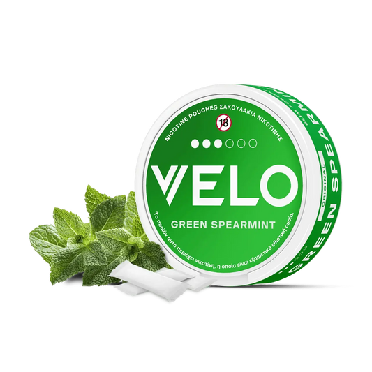 Ένα στρογγυλό πράσινο κουτί με την ένδειξη "VELO Green Spearmint" διαθέτει λευκό κείμενο, φύλλα μέντας και ένα σύμβολο "18+" στο καπάκι, επισημαίνοντας ότι πρόκειται για ένα σακουλάκι νικοτίνης μόνο για ενήλικες με φυτική βάση.