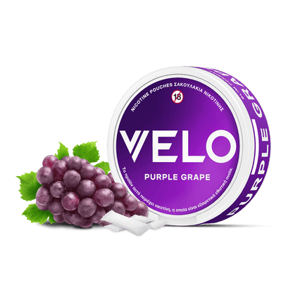 Ένα στρογγυλό δοχείο VELO Purple Grape βρίσκεται δίπλα σε ένα μικρό μάτσο σταφύλια και πράσινα φύλλα, με δύο λευκά φυτικά σακουλάκια νικοτίνης τοποθετημένα μπροστά.