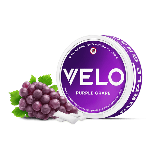 Ένα στρογγυλό δοχείο VELO Purple Grape βρίσκεται δίπλα σε ένα μικρό μάτσο σταφύλια και πράσινα φύλλα, με δύο λευκά φυτικά σακουλάκια νικοτίνης τοποθετημένα μπροστά.