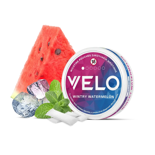 Ένα κουτί με σακουλάκια νικοτίνης VELO Wintry Watermelon βρίσκεται δίπλα σε μια φέτα καρπούζι, φύλλα μέντας, παγάκια και δύο λευκά σακουλάκια. Η ετικέτα του κουτιού είναι ροζ και μπλε.